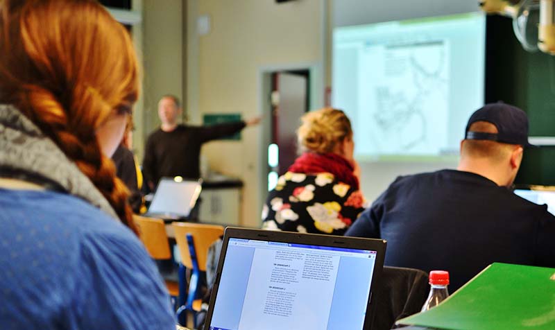 Foto af en underviser med powerpoint og mennesker, der lytter