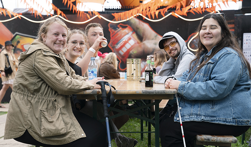 Deltagere fra sommertræf på Roskilde festival, sidder rundt et bord og hænger ud.