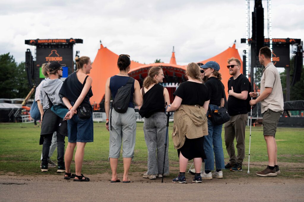 Ryggen af en gruppe unge foran orange scene på roskilde festival